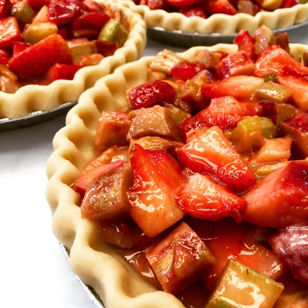 Several unbaked strawberry rhubarb pies with crimped crusts, ready for the oven.