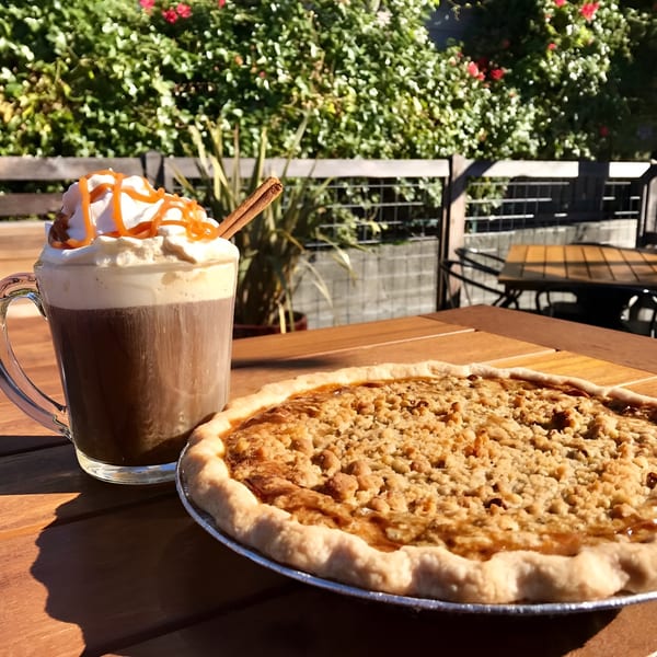 A Slice Of Humboldt Pie crumble pie and hot chocolate with whipped cream and caramel on a patio table.