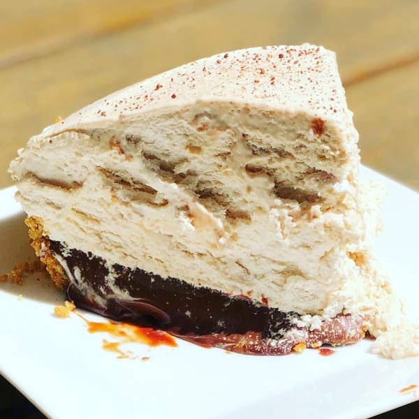 A slice of layered pie with a graham cracker crust, chocolate, and creamy filling.