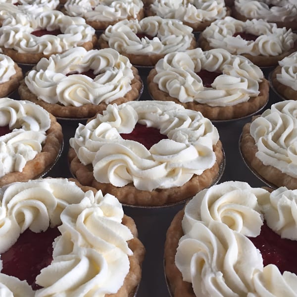 Rows of mini tarts with red filling and white whipped cream swirls from Slice Of Humboldt Pie.