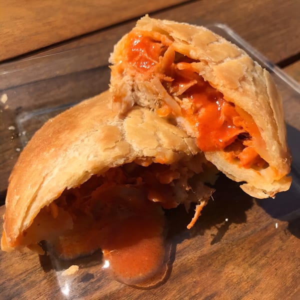 A golden-brown pastry, split open, revealing a vibrant orange, saucy filling with shredded ingredients.