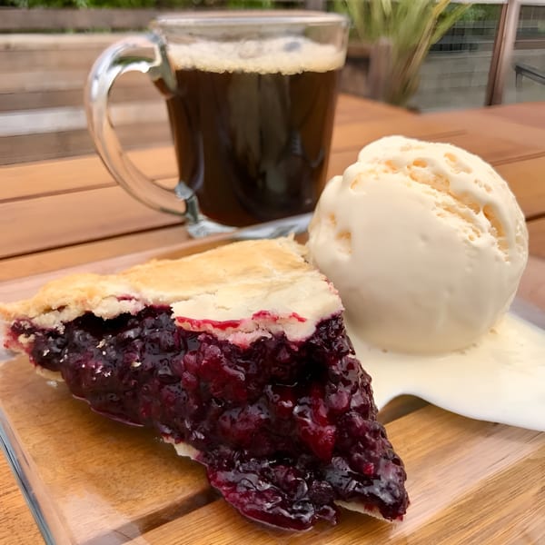 A slice of blueberry pie with a scoop of vanilla ice cream and a mug of coffee.